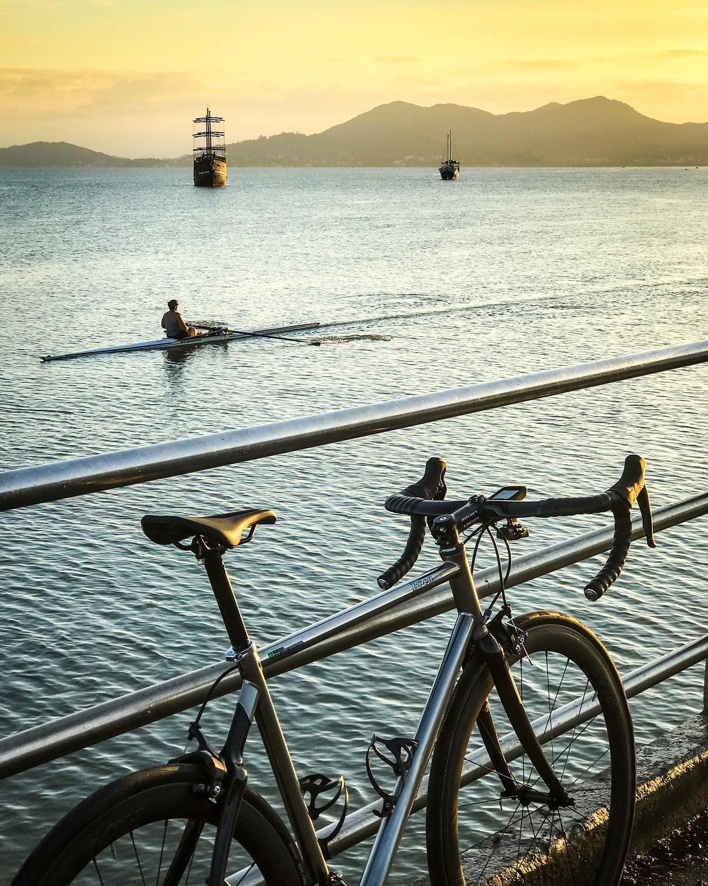 Bicicleta apoiada na grade da orla, com a baía ao entardecer